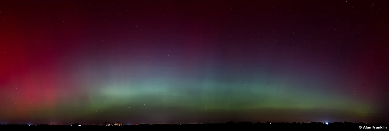 A wide band of green aurora stretches beneath a red northern sky.