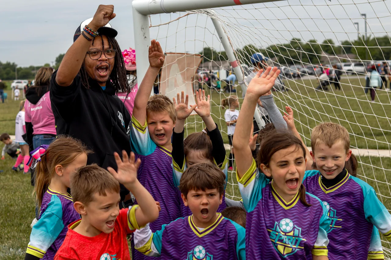 Young soccer players and their coach celebrate together with raised hands.
